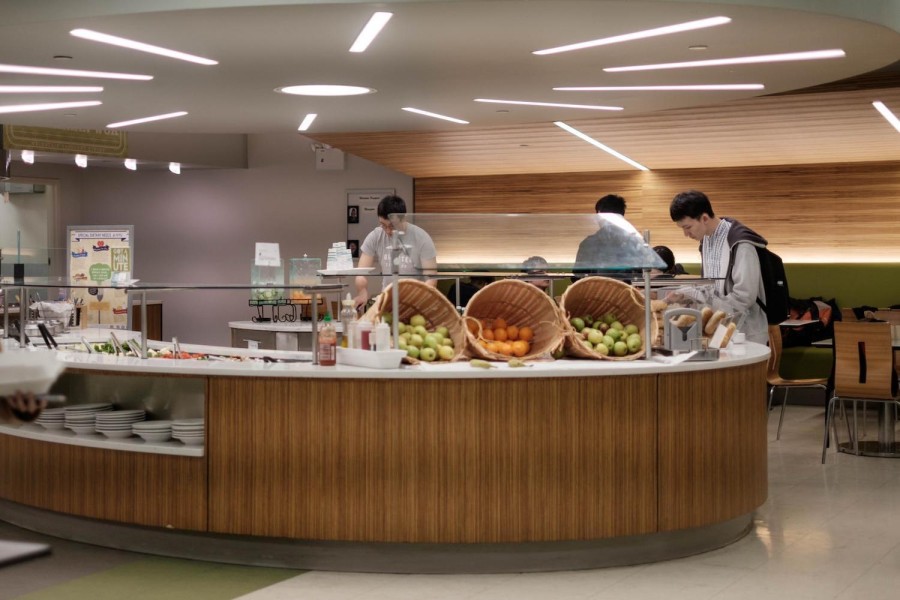 Two students at a salad bar with dining tables to the right.